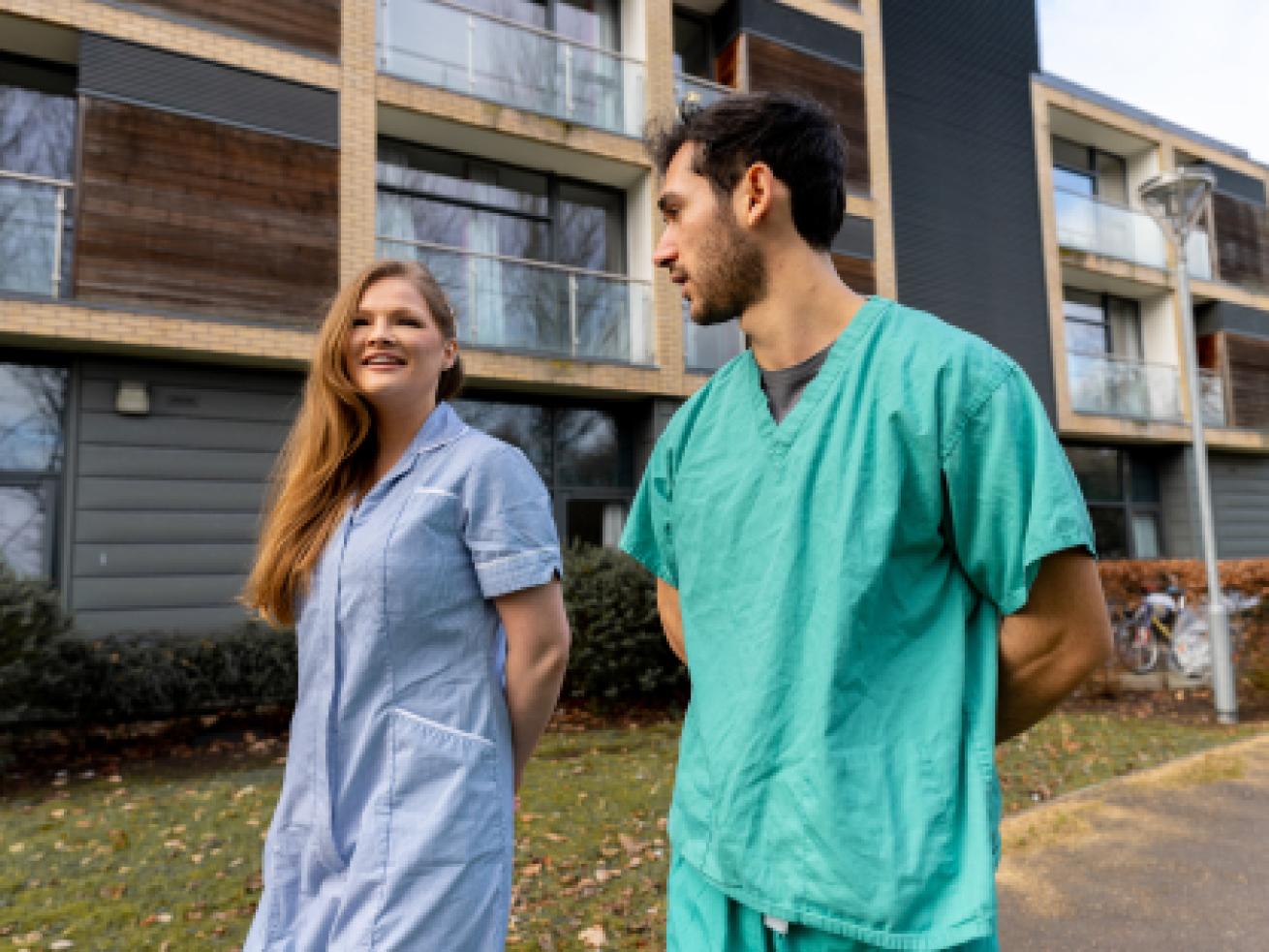 Keyworker students wearing hospital scrubs standing in front of a housing block