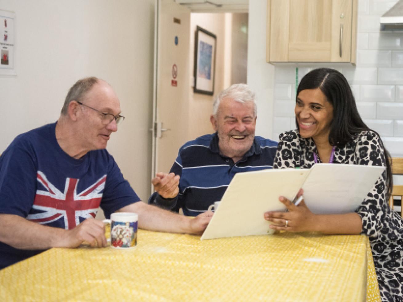 Sanctuary Supported Living staff and residents sat at a kitchen table looking at a binder and smiling